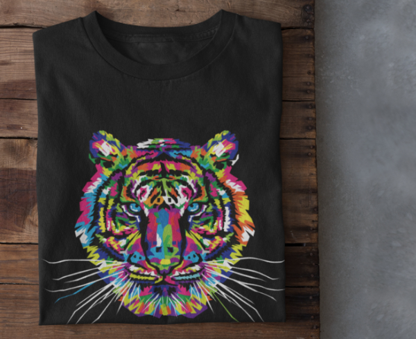 A black t-shirt with a tiger face composed of a rainbow of colors laying on a wooden table.