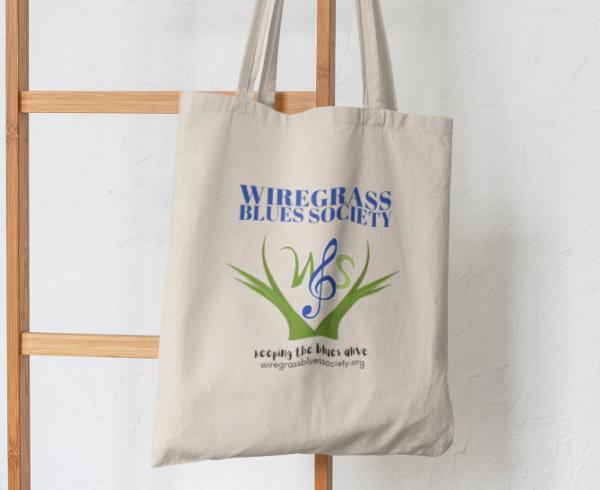 A natural cotton tote bag printed with a multi-color logo hangs against a white wall.